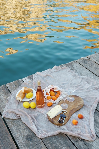 Frutas de vino rosado y bocadillos en el muelle de madera durante un pintoresco picnic en el muelle de madera