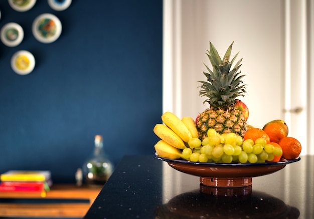 Foto fruteira fresca no interior moderno perto da parede azul escura na cozinha, bela casa de design moderno. abacaxi banana e frutas diversas