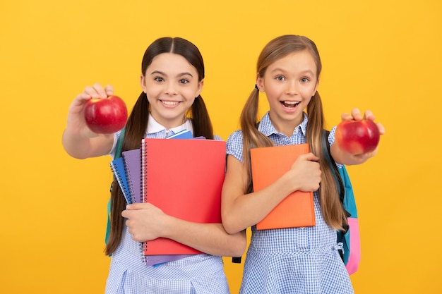 Fruto del conocimiento. Chicas adolescentes felices con libros muestran manzanas. Conocimientos alimentarios. Educación nutricional en la escuela. Fuente natural para una dieta saludable.