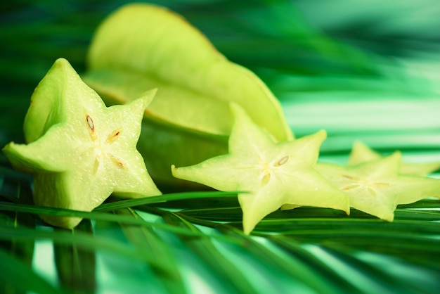 Fruto de estrela exótico ou carambola do averrhoa sobre as folhas de palmeira verdes tropicais no fundo de turquesa.