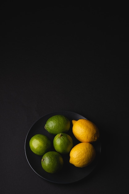 Frutos amargos de lima y limón en un plato negro sobre moody dark