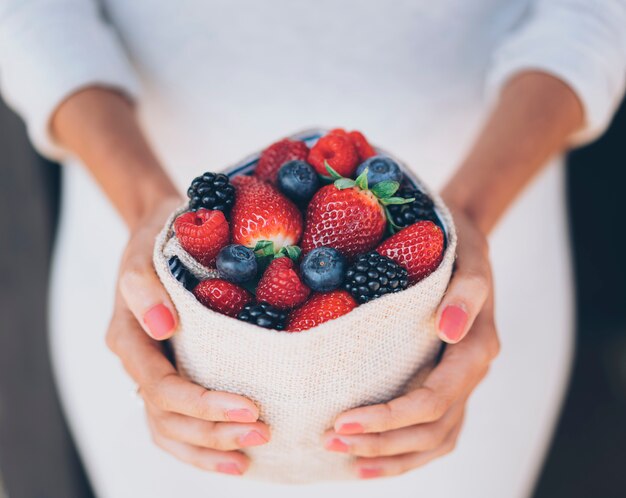 Frutos de bayas sanos y jugosos en manos de mujer con vestido blanco.