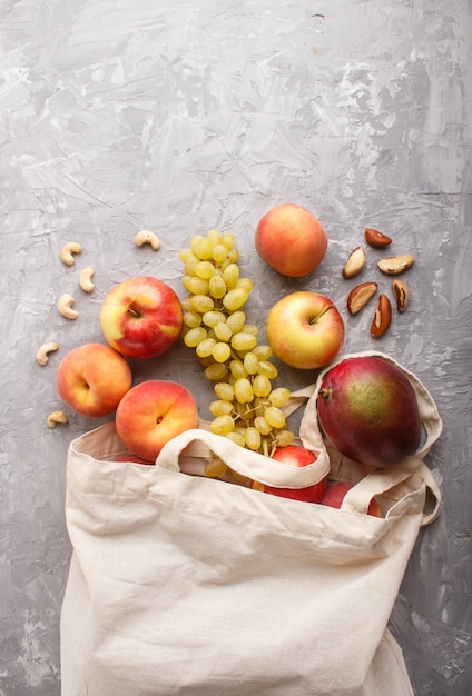 Frutos en bolsa de tela blanca de algodón reutilizable sobre hormigón gris. Cero residuos de compras, almacenamiento y reciclaje. Vista superior, endecha plana, copyspace.