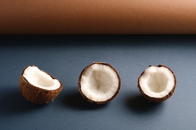 Frutos de coco en la superficie de papel doblado marrón y azul gris, concepto abstracto de alimentos tropicales, espacio de copia de vista de ángulo