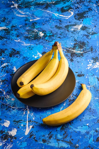 Frutos de banana em chapa preta sobre fundo azul texturizado, espaço de cópia de vista de ângulo