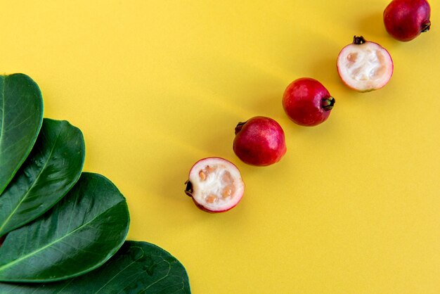 Frutos de goiaba cereja vermelha e folhas em fundo amarelo Psidium Cattleyanum