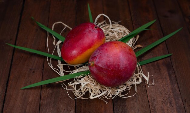 Frutos de manga com folhas em palha e mesa de madeira