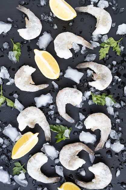 Frutos do mar com limão, salsa e gelo na superfície escura congelados camarões crus camarões no fundo de pedra preta serviram comida preparando comida saudável cozinhando dieta nutrição conceito vertical vista superior