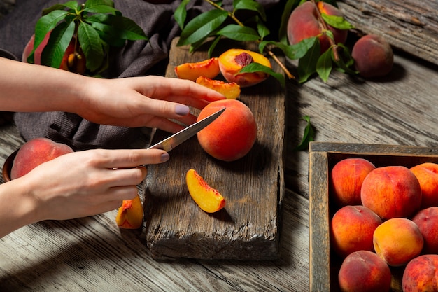 Frutos inteiros de pêssegos com folhas, pêssegos ao meio, fatias de pêssego na mesa de madeira. O processo de fazer geléia de pêssego, cozinhar a sobremesa de pêssego em uma tábua rústica por mãos femininas. Humor negro