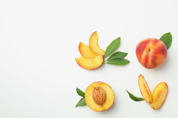 Frutos maduros de durazno con hojas sobre fondo blanco.