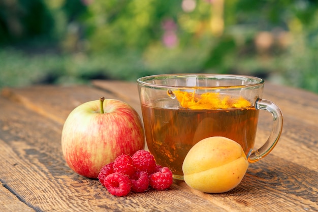 Frutos maduros de manzana, albaricoque y frambuesas y taza de té verde con flores de caléndula.