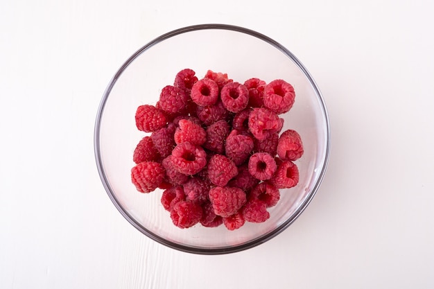 Frutos rojos de frambuesa en recipiente de vidrio transparente sobre superficie blanca