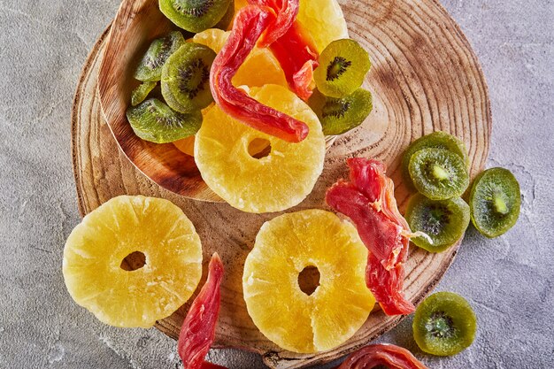 Foto frutos secos: anillos amarillos de piña confitada, papaya roja y kiwi verde sobre una tabla de madera