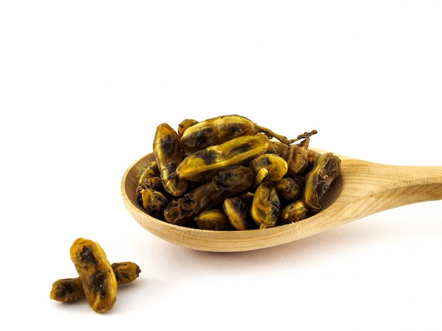Frutos secos de Sophora japonica se encuentran en una cuchara de madera sobre un blanco