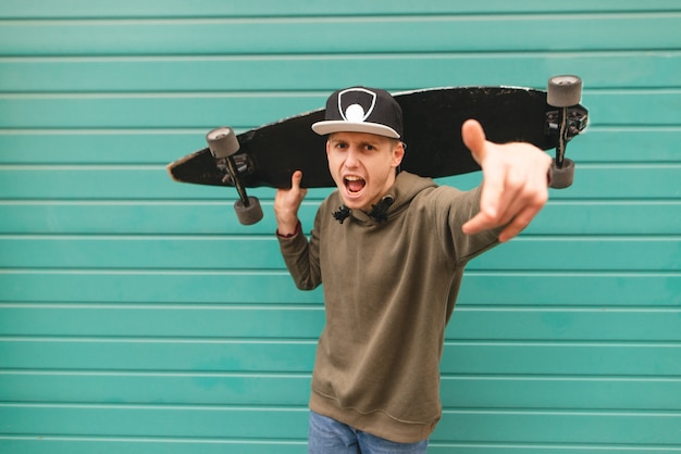 Foto fstylish junger mann in straßenkleidung, hält ein longboard