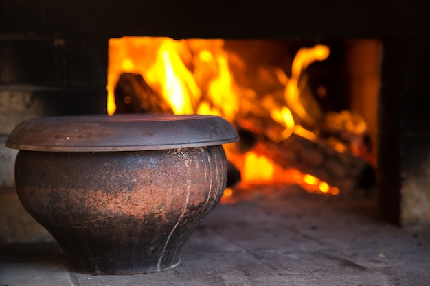 El fuego en el antiguo horno tradicional pueblo ruso en un estilo rústico. Olla de sopa cerca de la leña