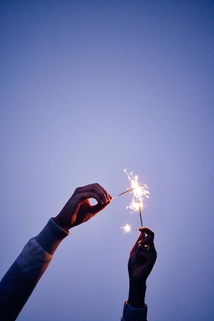 Fuego de bengala y manos de una persona en una celebración de cielo azul con luz y fiesta al aire libre en la noche Color creativo y mujer con fuegos artificiales para celebrar en la naturaleza durante la puesta de sol en año nuevo