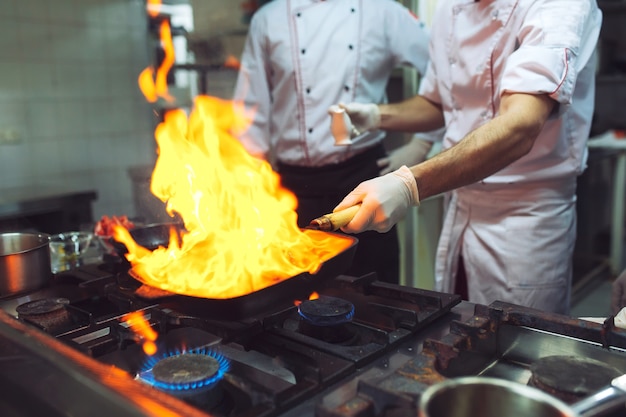 Fuego en la cocina. La quema de gas de fuego se está cocinando en una sartén de hierro, revuelva el fuego muy caliente