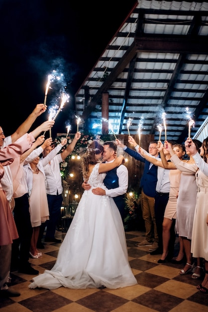 Fuego frío de velas de pastel y fuegos artificiales en manos de las personas que rodean a los recién casados.