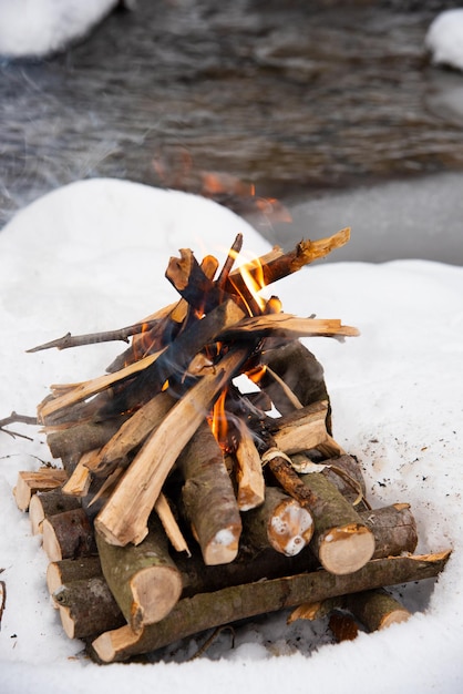 Fuego en la nieve cerca del arroyo de montaña en el bosque de invierno Paisaje de invierno