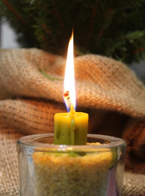 Fuego de vela de cera amarillo oscuro en candelabro de vidrio lleno de granos cerca de la envoltura de burlap hecha a mano