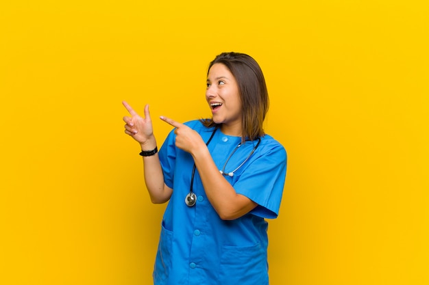 Fühlen Sie sich fröhlich und überrascht, lächeln Sie mit einem schockierten Ausdruck und zeigen Sie auf die Seite, die gegen die gelbe Wand isoliert ist