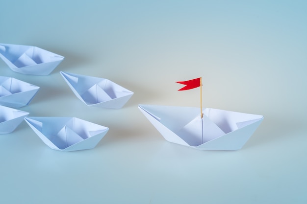 Führungskonzept unter Verwendung des Papierschiffs mit roter Fahne auf blauem Hintergrund