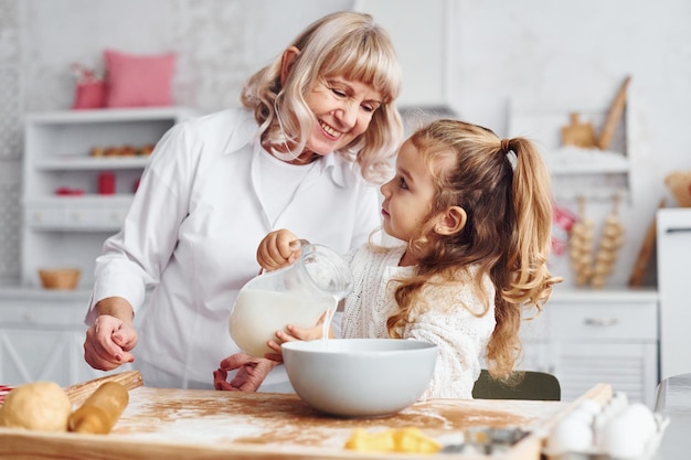 Füllt sich mit Milch Ältere Großmutter mit ihrer kleinen Enkelin kocht Süßigkeiten für Weihnachten in der Küche