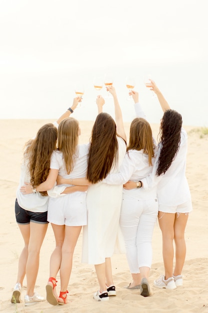 Fünf Mädchen umarmen sich am Strand und trinken Coctails