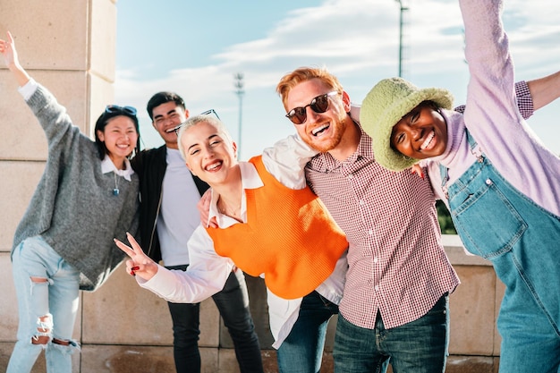 Fünf multiethnische Freunde posieren lächelnd vor der Kamera und haben gemeinsam Spaß im Freien