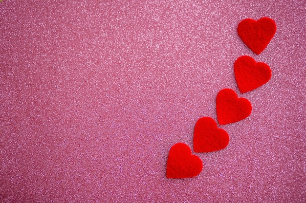 Fünf rote Herzen auf einem rosa glänzenden Hintergrund am Valentinstag