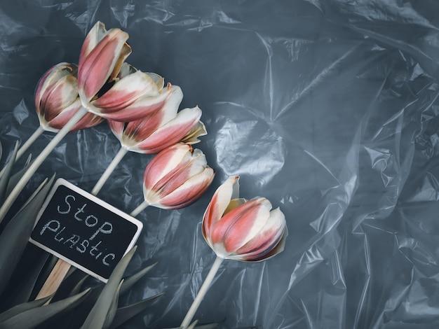 Fünf verwelkte Tulpen und ein Pflock mit der Aufschrift Stop Plastic liegen links auf einer Plastiktüte