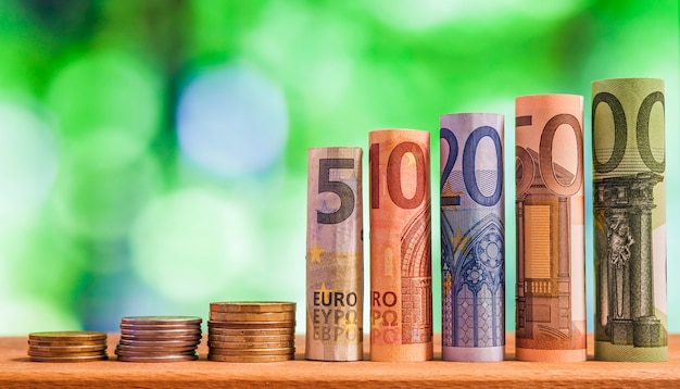 Fünf, zehn, zwanzig, fünfzig und hundert Euro rollten Rechnungsbanknoten, mit Euromünzen auf Grün unscharfem bokeh Hintergrund.