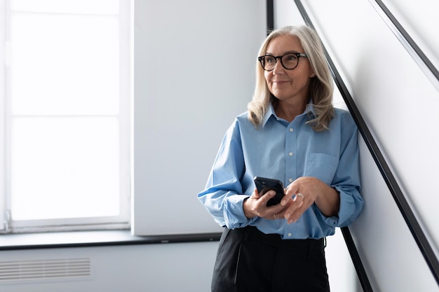 Fünfzig Jahre alter erfolgreicher Frauenkopf mit Handy im Büro