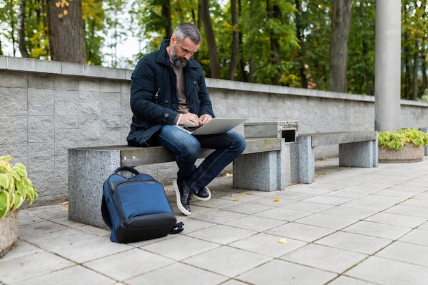 Fünfzig Jahre alter Mann, der online im Stadtpark am Laptop arbeitet