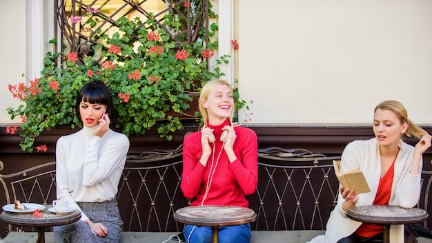 Fuente de información. Ocio femenino. Fin de semana relax y ocio. Pasatiempo y ocio. Intereses diferentes. Grupo de mujeres bonitas en la terraza del café se entretienen leyendo, hablando y escuchando.