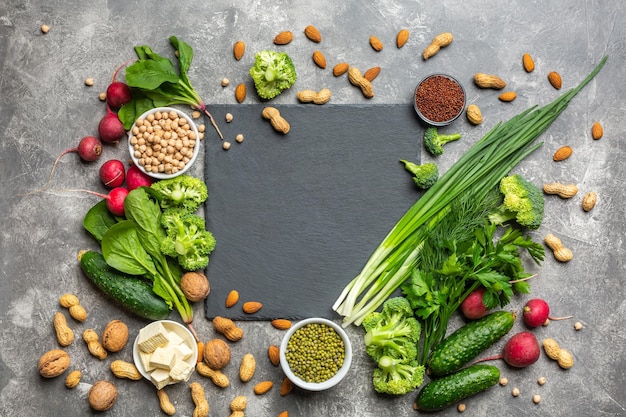 Una fuente de proteína para vegetarianos. Alimentos sanos y limpios: verduras, verduras, nueces y legumbres vista superior sobre un fondo de hormigón con una piedra cortante negra en el centro.