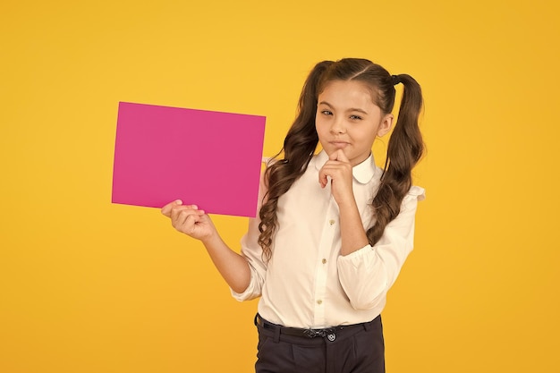 Für Schulinformationen Kleines Kind, das leeres rosafarbenes Papier für Informationen auf gelbem Hintergrund hält Kleines Mädchen mit Hinweis auf Informationen Verbreitung von Informationen und Sammeln von Wissen kopieren Raum