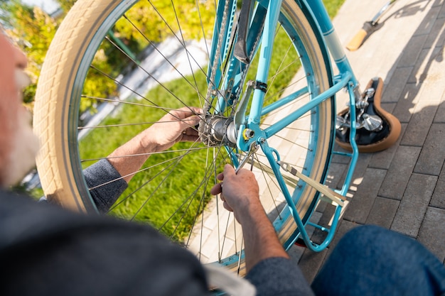 Fuera de casa. Vista superior del hombre maduro, reparación de bicicleta azul antigua fuera de la casa de verano