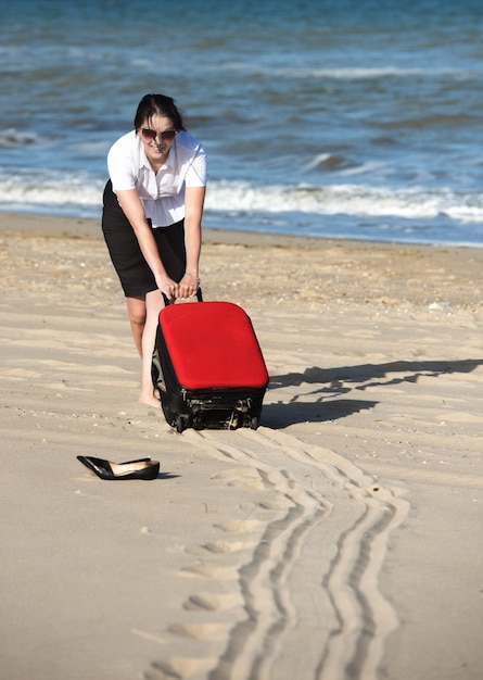 Fuera de la oficina de vacaciones en el mar La mujer arrastra la maleta sobre las arenas hasta la playa