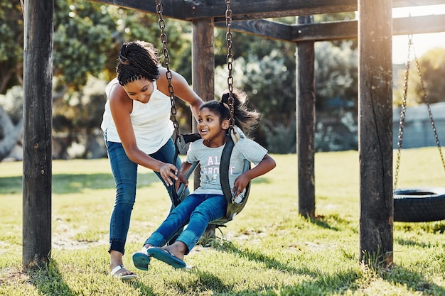 Fuera por un poco de sol y diversión Toma completa de una madre empujando a su hija en un columpio en el parque