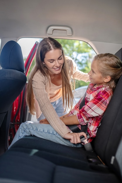 Fürsorgliche Mutter, die den Sicherheitsgurt ihrer Tochter auf dem Rücksitz des Autos anschnallt