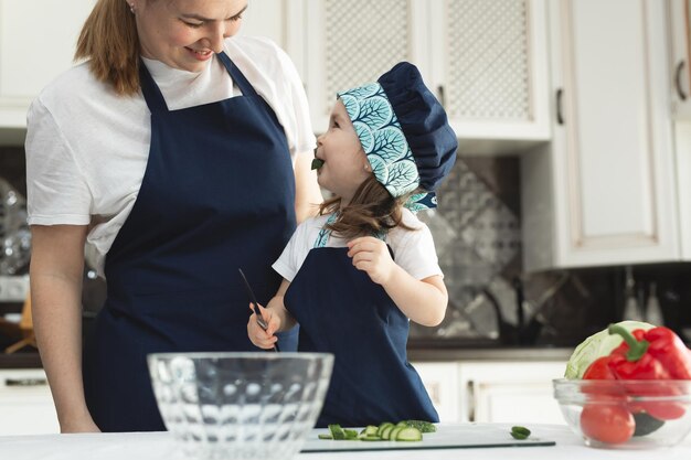 Fürsorgliche Mutter, die der kleinen Tochter beibringt, Salat in der Küche zu kochen
