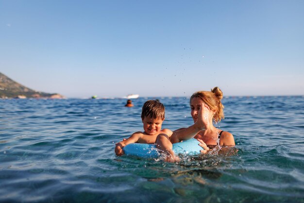 Fürsorgliche Mutter reitet ihren Sohn auf einem aufblasbaren Ring im Meer