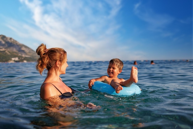 Fürsorgliche Mutter reitet ihren Sohn auf einem aufblasbaren Ring im Meer