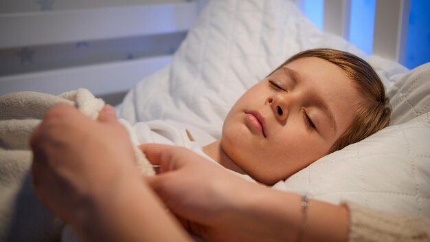 Fürsorgliche Mutter rückt die Decke zurecht und küsst nachts ihren schlafenden kleinen Sohn