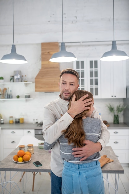 Fürsorglicher nachdenklicher Vater, der seine Tochter in der Küche fest umarmt.