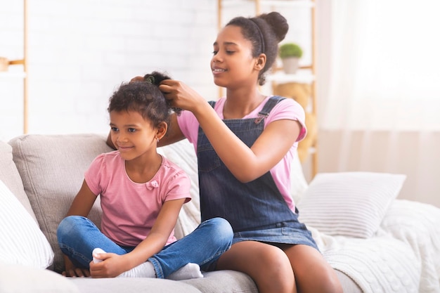 Fürsorgliches afrikanisches Teenagermädchen, das zu Hause die Haare seiner kleinen Schwester bürstet