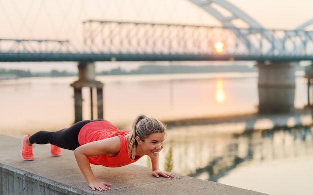 Fuerte ajuste chica rubia haciendo flexiones fuera. Entrenamiento matutino de principios de verano.