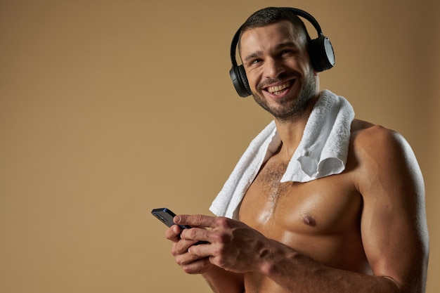 Fuerte atleta divertido con auriculares posando a la cámara en estudio